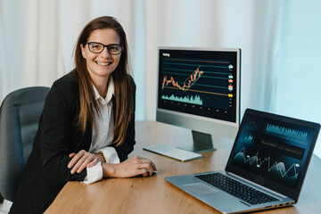 Female trader at table with laptop and computer monitor