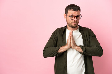 Young Brazilian man isolated on pink background keeps palm together. Person asks for something