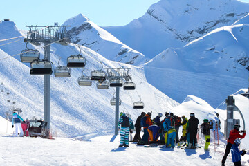 A crowd of skiers and snowboarders on the ski slope in front of the chairlift. People put on...