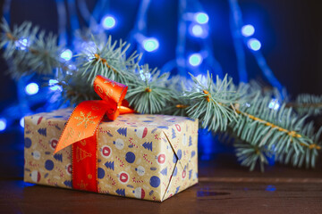 Christmas gift box with red ribbon near fir pine tree branch on blue background. Christmas concept