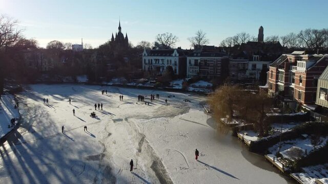 Ice skating people on a frozen canal in the city center of Zwolle during a beautiful winter day in Overijssel, The Netherlands. Aerial drone point of view.