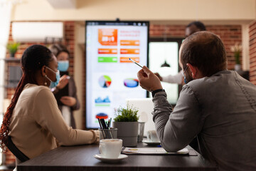 Business managers showing management presentation working at company strategy with businessteam in startup office. Diverse group of people wearing medical face mask to prevent infection with covid19