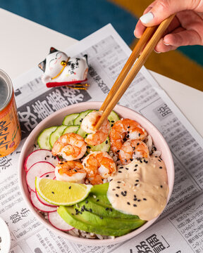 Bowl With Shrimps, Cucumbers, Radishes, Avocado, Sesame Seeds And Auce On The Background Of A Japanese Newspaper