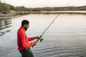 Smiling man fishing in lake during sunset