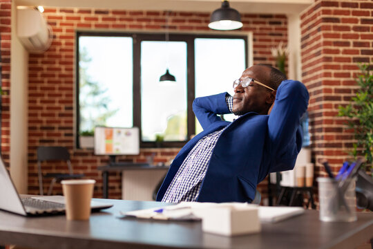 Business man relaxing after finishing task, taking break in startup office. Employee feeling carefree, sitting with hands over head to relax and daydream after job is done. Peaceful adult