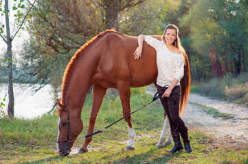 Portrait of young beautiful woman with brown horse at summer green park.