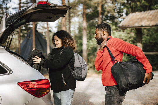 Multiracial couple loading luggage in car trunk during vacation