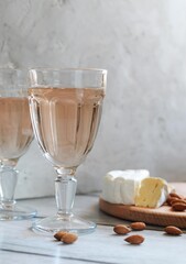 Two glasses of rose wine with brie cheese and almonds on the light concrete background. Vertical orientation.
