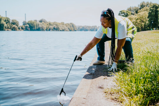 Mature female volunteer cleaning plastic with claw from lake