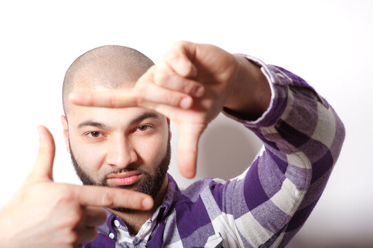 Interested young bearded man focusing on you while standing against white background.