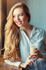 Drinking latte. Young beautiful long hair woman holding cup of coffee while sitting at cafe.