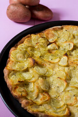Round pan of homemade pizza topped with sliced potatoes, salt, oil and oregano on a pink background