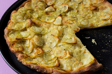 Round pan of homemade pizza topped with sliced potatoes, salt, oil and oregano on a pink background