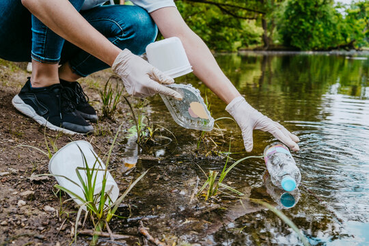 Low section of female volunteer cleaning plastic waste from pond at park