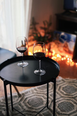 Two glasses of red wine on a black table in a living room, garland lights on the background, Christmas winter mood