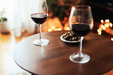 Two glasses of red wine on a wooden table at home, Christmas lights 