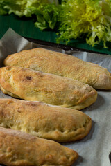 Panzerotti with escarole and grana padano baked in the oven with parchment paper. Close-up of panzerotti on green wood background and smooth and curly endive tufts in the background