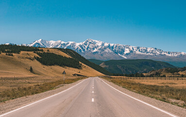 Fototapeta premium Empty asphalt road in front of huge majestic mountains with snow covered peaks. Beautiful landscape of Altay region, Russia.
