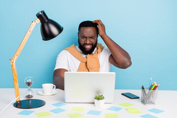 Photo of troubled guy sit table pc try solve dilemma wear t-shirt jumper front-tie isolated blue...