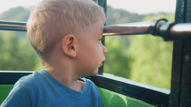 Surprised little boy enjoys picturesque landscape sitting in poma lift cabin at highland resort on nice summer day extreme close view