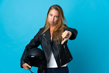 Middle age woman holding a motorcycle helmet isolated on blue background showing thumb down with negative expression