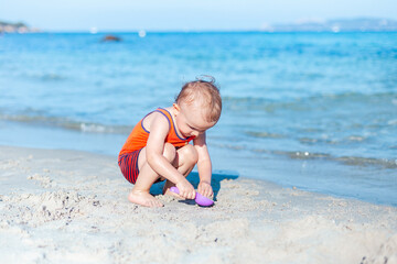 Little toddler boy playing with sand on a beach. Child wearing sun protection clothes. Summer vacation in France. Holidays with children concept, copy space.
