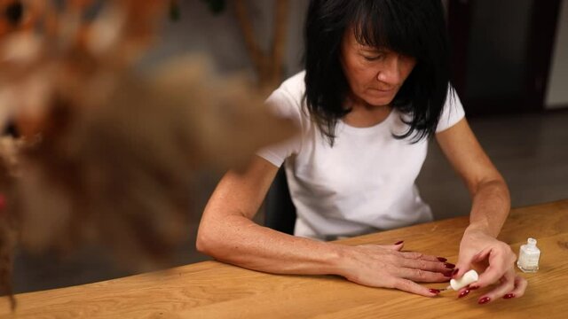 Senior woman applying polish on nails at home, aged female painting fingernails with colorless protective enamel, Beauty treatment and hand care concept