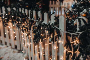 Wooden fence decorated with golden garlands and New Year's branches in the snow