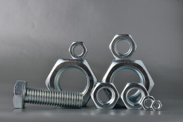 composition of new bolts and nuts of different sizes on a gray background.