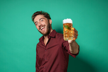 Cheerful young man looking at the camera cheering with a glass of beer - isolated on a green-bluish...