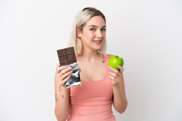 Young caucasian woman isolated on white background taking a chocolate tablet in one hand and an...