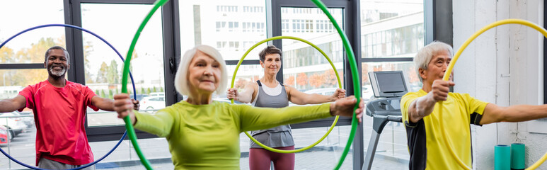 Smiling multicultural people exercising with hula hoops in gym, banner.