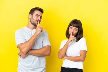 Young couple isolated on yellow background showing a sign of closing mouth and silence gesture