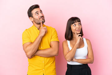 Young couple isolated on pink background thinking an idea while looking up