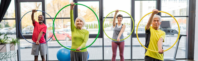 Group of multiethnic elderly people training with hula hoops in sports center, banner.