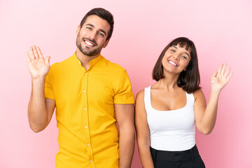 Fototapeta na wymiar Young couple isolated on pink background saluting with hand with happy expression