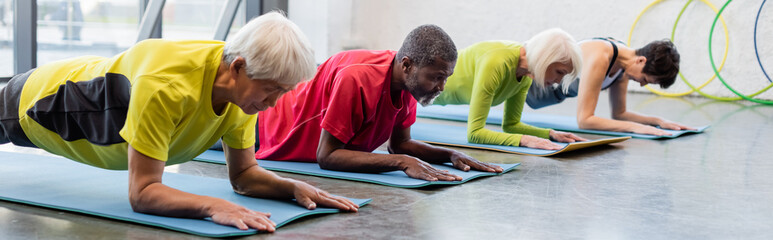 Multiethnic senior people training on fitness mats in gym, banner.