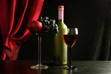 A glass of red wine, a bottle and a bunch of grapes in a high vase against a background of burgundy curtains.