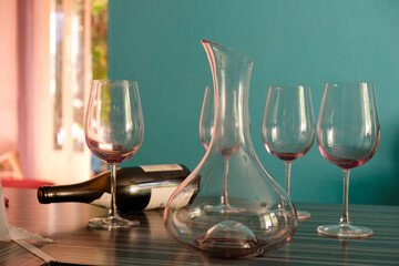 An empty wine carafe, four glasses, and an empty bottle in the sunny kitchen in the evening golden hour. Light sea green color background. 