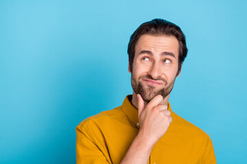 Photo of thinking millennial brunet guy look empty space wear yellow shirt isolated on blue color background