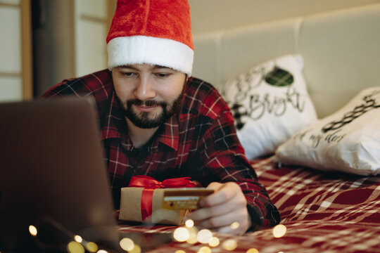 Man In Red Plaid Flannel Shirt In Santa Hat Shopping Online For Christmas Present Paying With Golden Debit Card