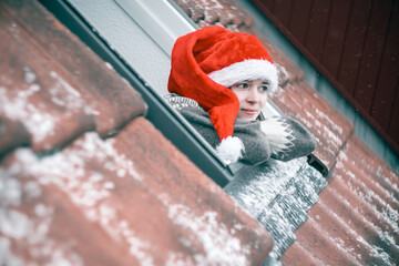 Young woman in a red and white Christmas hat looking out of a skylight window waiting for a miracle...