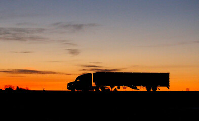 This image of a large transport truck silhouetted by the sunrise indicates that the transportation...