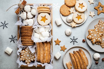 Fototapeta na wymiar Gift wooden box with tasty homemade cookies, marshmallows and meringue on gray background. Christmas and New Year concept. Gingerbread, austrian linzer cookies, biscotti. Top view, holidays flat lay.
