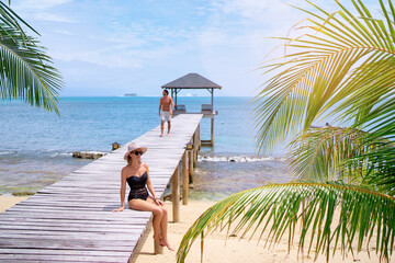 Luxury lifestyle and vacation. Tanning and sunbathing on the beach. Young womanand man in swimwear enjoying sea view on wooden pier.