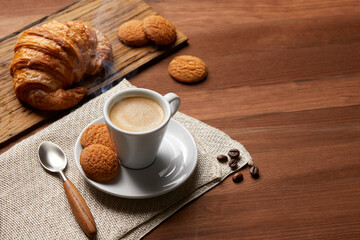 A cup of coffee and a croissant on a wooden table
