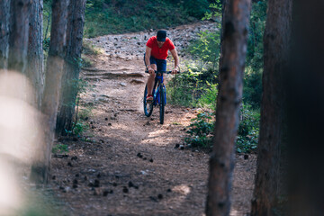 Obraz premium Fit cyclist riding his bike downhill through a forest ( woods ) while wearing a red shirt and red shoes.