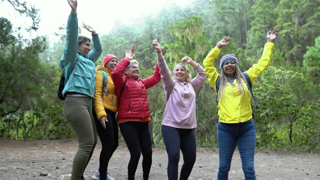 Group of women with different ages and ethnicities having a funny moment dancing during a walk in the woods - Adventure and travel people concept 