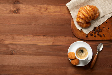 A cup of coffee and a croissant on a wooden table