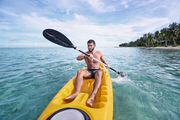 Young man paddling the sea kayak in the tropical bay.